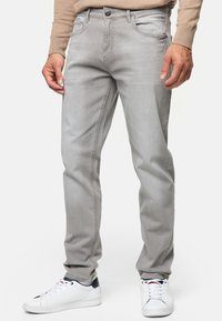 Grijze denim jeans met een rechte pasvorm, vijf zakken en een knoopsluiting. Draagt met witte sneakers met zwarte accenten.