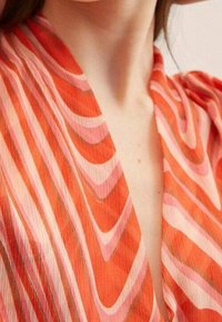 Abito in tessuto con profondo scollo a V e motivi a onde orizzontali nei colori arancione, rosa e crema; tessuto leggero e testurizzato.