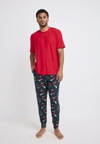 Rode t-shirt met korte mouwen gecombineerd met donkerblauwe pyjamabroek met een patroon van skifiguren en feestelijke elementen. Gemaakt van een katoenmix.