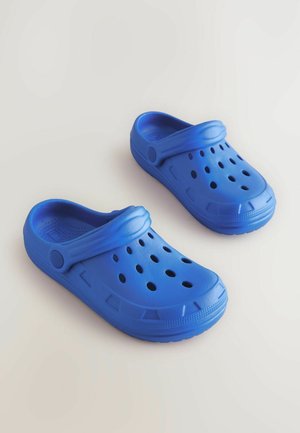 Blå lätta träskor med ventilationshål, upphöjd kant och avtagbar rem för säker passform. Tillverkade av ett mjukt, hållbart material.