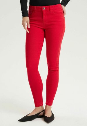 Czerwone spodnie o wąskim kroju noszone z czarnymi, spiczastymi balerinami typu slingback i czarnym topem z długim rękawem, pokazane od talii do stóp.