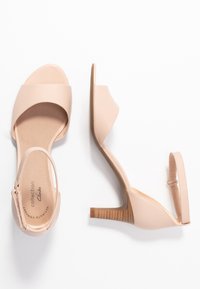 Sandales à talons nues avec une tige synthétique brillante, design ouvert à l'avant, bride de cheville ajustable et talon carré en bois texturé.