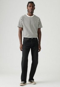 Gestreepte t-shirt met korte mouwen in crème en zwart, gecombineerd met zwarte rechttoe-rechtaan jeans en beige sneakers. Eenvoudig ontwerp, casual pasvorm.