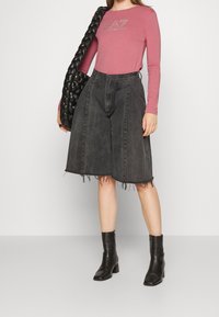 Långärmad rosa topp med silverlogotyp, matchad med en knälång svart denimkjol med fransad fåll och svarta ankelboots.