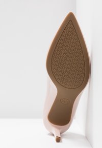 Semelle d'une chaussure à talon aigu en cuir verni nude avec un motif de logo Michael Kors sur la semelle en caoutchouc, sur fond blanc dans un coin.