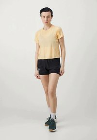 Kratki rukavi, skraćeni žuti majica uparena s crnim sportskim kratkim hlačama. Model nosi zelene tenisice i bijele čarape do gležnja. Jednostavan dizajn.