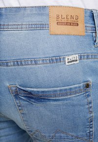 Světle modré džínové kalhoty s hnědou koženou štítkem na pase a bílou látkovou štítkem u zadní kapsy. Viditelné švy.