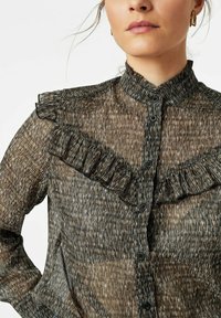 Sheer black blouse with a textured, abstract pattern, featuring a ruffled yoke and a high collar, fastened with black buttons.