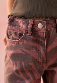 Rot-orange Denim-Jeans mit einem Zebra-Print-Muster, einer vorderen Tasche und einem Metallknopf-Detail am Bund. Texturierter Stoff.