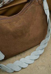 Hnedá semišová kabelka s opleteným svetlomodrým remienkom, vybavená zipsovým uzáverom a jemným reliéfnym vzorom na povrchu.