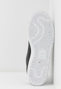 Svart skosula med en texturerad vit gummiyta som har ett bikupemönster och färgglada prickar; Adidas-logotypen präglad.