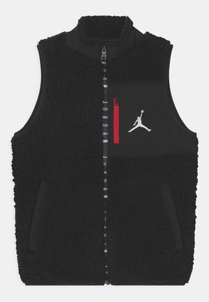 Veste sans manches noire en sherpa avec fermeture éclair avant, poche poitrine avec fermeture éclair rouge et logo Jumpman blanc sur la poche poitrine.