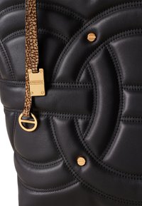 Borsa a spalla nera in pelle con design circolare trapuntato, hardware dorato e una distintiva tracolla marrone decorata, fissata con un gancio metallico.