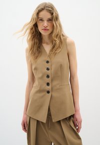 Gilet senza maniche color sabbia con scollo a V, dotato di sei bottoni neri sul davanti, cuciture ordinate e tasche angolate.