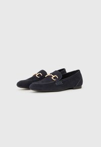 Marineblå mokkasiner i semsket skinn med en gullfarget hestesko-applikasjon, flat såle og sydd detaljer langs kantene. Klassisk slip-on design.