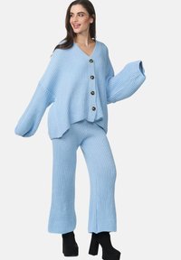 Ensemble tricot léger bleu clair comprenant un cardigan ample avec quatre boutons et un pantalon évasé assorti, présentant une texture côtelée.