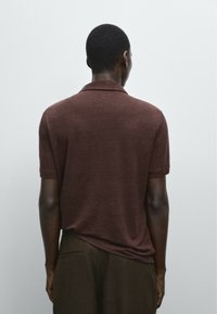 Polo shirt marrone a maniche corte realizzato in materiale morbido, con colletto e vestibilità comoda, abbinato a pantaloni scuri.