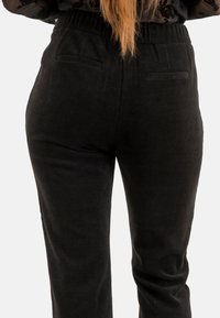 Pantaloni in corduroy neri con una finitura testurizzata, dotati di una vita alta e due tasche posteriori. Taglio dritto, dettagli minimi.