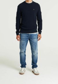 Granatowy sweter dziany o prążkowanej fakturze, z okrągłym dekoltem i małym logo; w połączeniu z jasnoniebieskimi postrzępionymi dżinsami i szarymi tenisówkami.