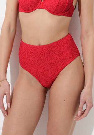 Donna che indossa slip bikini rossi a vita alta con motivo floreale testurizzato e reggiseno rosso abbinato con ferretto.