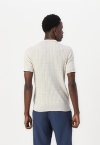 Ljusgrått stickat tröja med korta ärmar, prydd med ett texturerat kabelmönster och ribbad nederkant. Bärs tillsammans med mörkblå byxor.