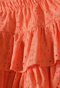 Tissu corail froncé arborant des motifs floraux brodés et des découpes. La texture est légère et légèrement froissée.