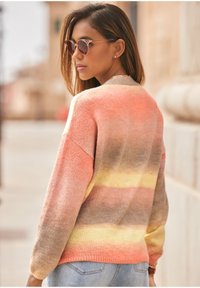 Stickad tröja med gradientrandiga mönster i rosa, orange och gult. Avslappnad passform med långa ärmar och ribbad nederkant, kombinerad med denimjeans.