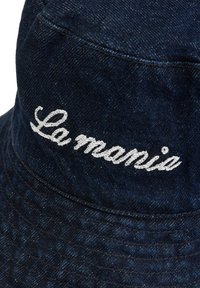 Sötétkék farmerkalap, az elején hímzett fehér "La mania" felirattal. Texturált anyagból készült, széles karimával rendelkezik.