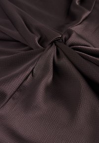 Mørkebrun stof med en struktureret overflade, der har bløde fald og milde folder. Materialet virker glat og let blankt.