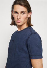 Ναυτικές μπλε μπλούζα με γιακά σε στυλ crew neck και κοντά μανίκια, με διακριτό λογότυπο στο στήθος και εμφανή λεπτομέρεια ραφής κατά μήκος των ραφών.