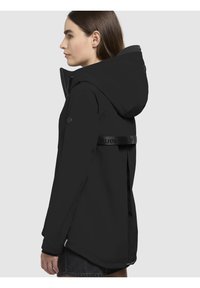 Zwarte waterdichte jas met capuchon, voorzien van een ritssluiting, zijzakken en een gelogd bandje op de rug. Glad textuur en modern ontwerp.
