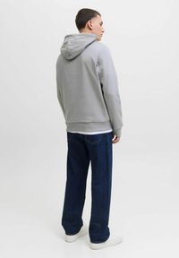 Sudadera gris con capucha de textura suave, combinada con jeans de corte recto azul oscuro y zapatillas blancas, vista desde atrás.