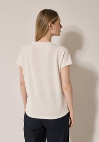 Top corto a maniche corte beige chiaro con finitura testurizzata e scollatura rotonda, con maniche arrotolate e una vestibilità rilassata lungo l'orlo.