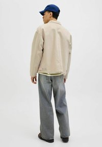 Beige oversized jacket with a collar, denim pants, and brown shoes. A blue cap completes the look. Simple, casual design with loose fit.