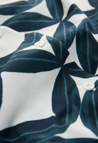 Tissu blanc avec de grands motifs floraux abstraits bleu foncé et des boutons blancs sur une surface douce légèrement froissée.