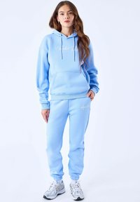 Sweat-shirt bleu clair avec capuche et cordons, doté d'une poche avant. Pantalon de survêtement assorti avec poignets élastiques, les deux en tissu doux.