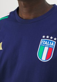 Granatowa koszulka bawełniana z białym i zielonym emblematem włoskiej flagi, cztery gwiazdki powyżej i złota gwiazdka z boku.