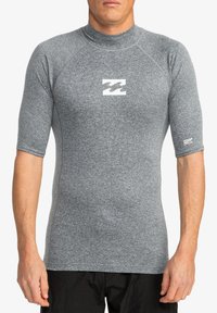 Rash guard gris de manga corta con un diseño ajustado, fabricado con material texturizado, que presenta un logo blanco en el pecho y una marca en la manga.