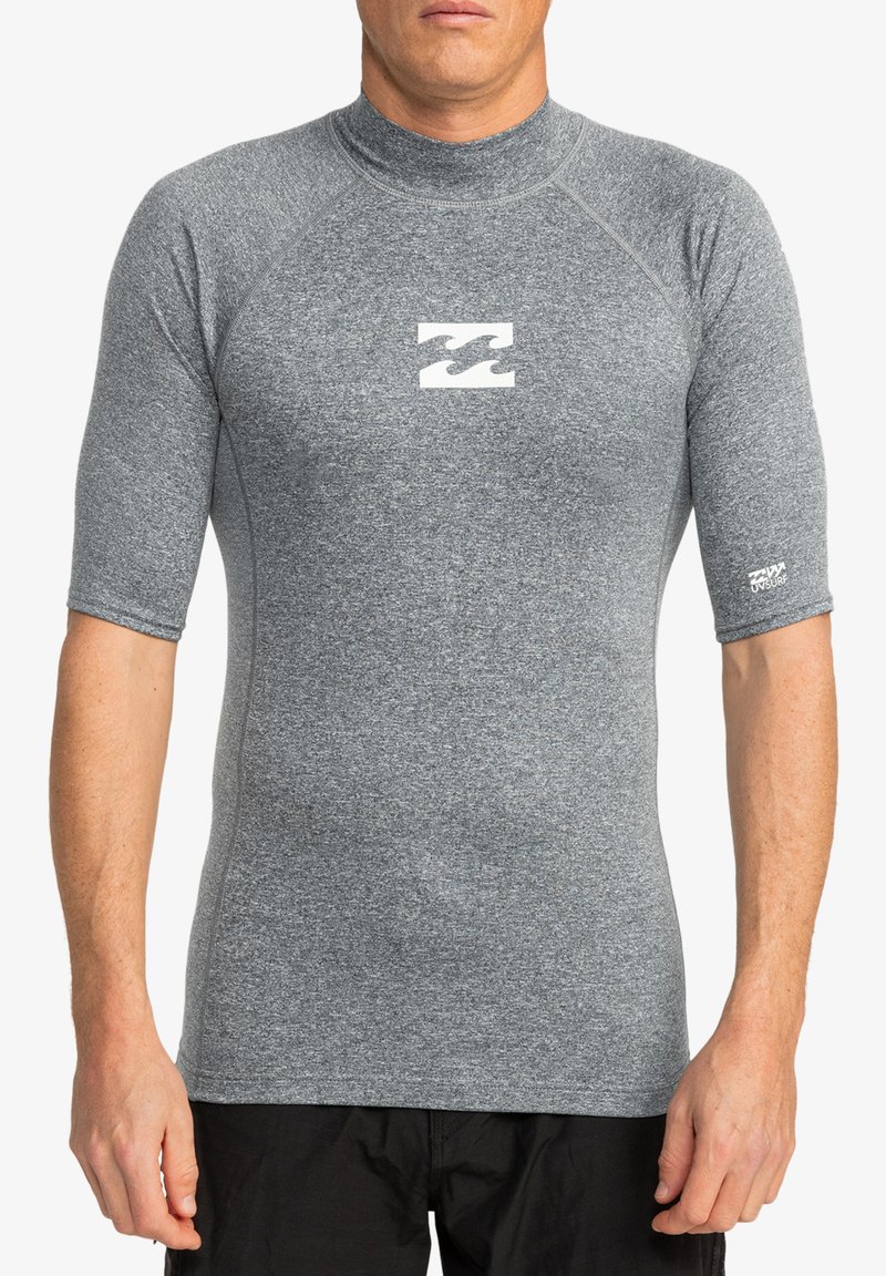 Rash guard gris de manga corta con un diseño ajustado, fabricado con material texturizado, que presenta un logo blanco en el pecho y una marca en la manga.