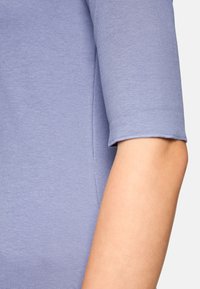 Helllila gestricktes Oberteil mit glatter Textur, ausgestattet mit Ärmeln in Ellbogenlänge und einem runden Ausschnitt. Einfaches Design, ohne Verzierungen.