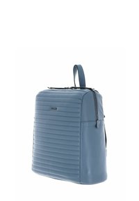 Sac à dos en cuir bleu avec texture striée, en forme carrée, avec une poignée supérieure et une fermeture éclair. Il présente un logo discret sur le devant.