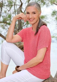 Koraal brei korte mouw trui met een textuurpatroon, gecombineerd met witte capri-broeken. Inclusief een houten armband om de pols.