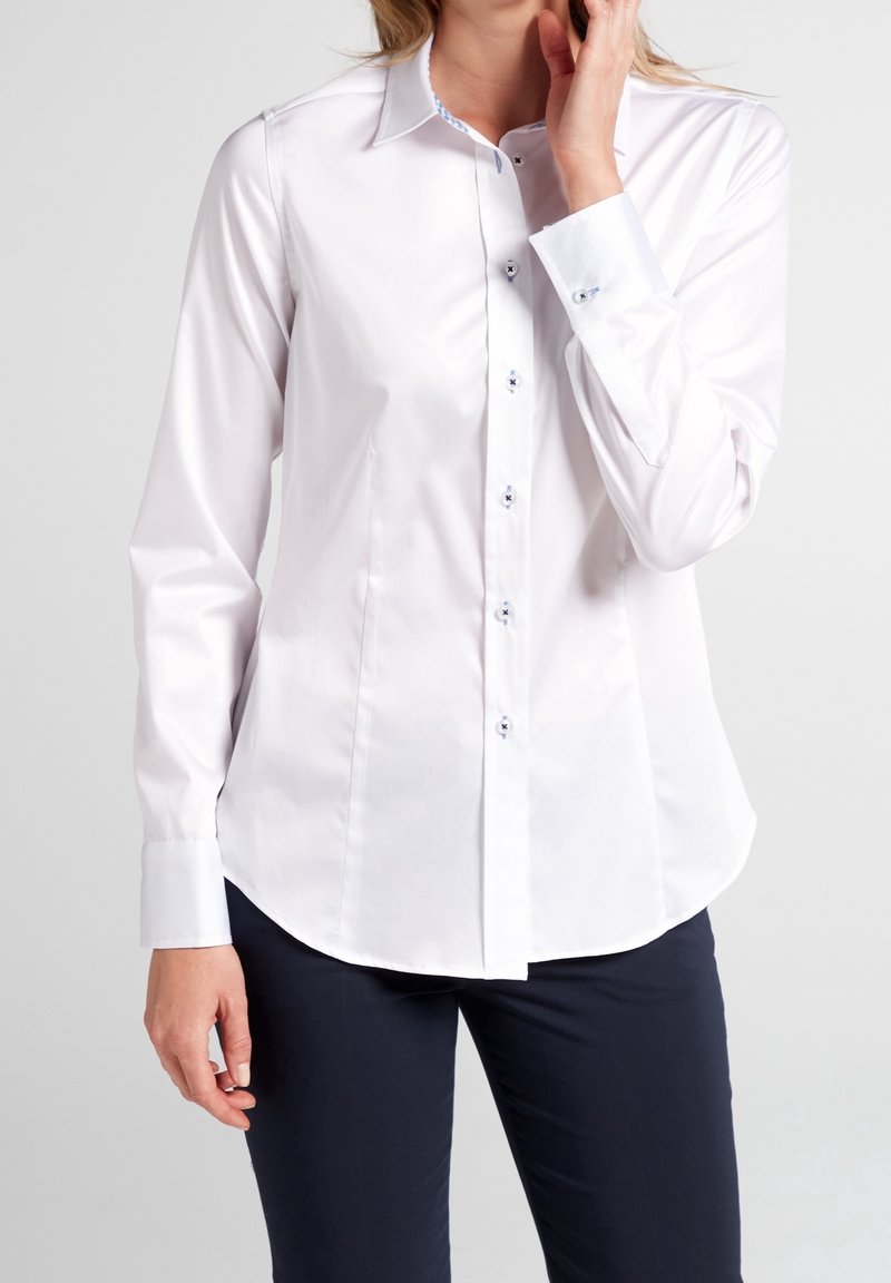Chemise blanche à manches longues avec un col classique, fermeture à boutons, ourlet arrondi et un motif bleu contrastant à l'intérieur du col et des poignets.