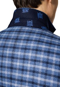 Niebieska koszula w kratę o teksturowanym wykończeniu; kontrastujący ciemnoniebieski kołnierzyk z dekoracyjnym niebieskim wzorem. Widoczne detale przeszyć.