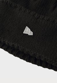 Sort strikket hue med ribbet tekstur, en foldet manchette og et sølvfarvet logo-tag med et geometrisk design på forsiden.