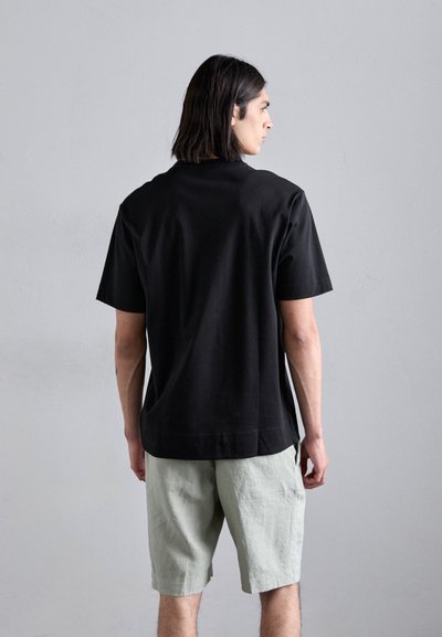 Sort T-shirt med kortærmer og løs pasform, lavet af blødt bomuld, kombineret med lysegrønne linnedshorts, synlige sømme og lige kant.
