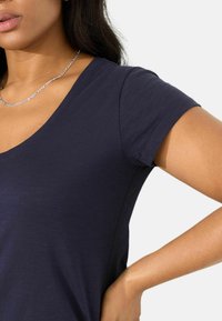 T-shirt a maniche corte blu navy con scollatura a V, realizzato in tessuto liscio, caratterizzato da una consistenza morbida e una silhouette aderente, con una leggera lucentezza.