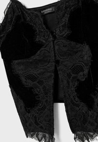 Black velvet vest with intricate lace detailing at the edges, featuring a button closure and a textured finish.