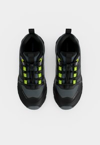 Paire de chaussures de sport noires et grises avec des boucles de lacets vert vif et des languettes de traction, vues de dessus sur fond blanc.
