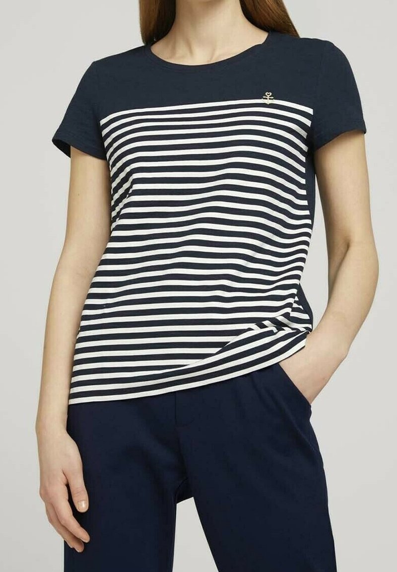 Tummansininen ja valkoinen raidallinen t-paita, jossa on lyhyet hihat ja pyöreä kaula-aukko; vasemmassa ylärintakehässä on pieni ankkurimerkki.